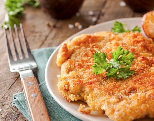 Wiener Schnitzel with roasted potatoes and lemon slice on a plate.