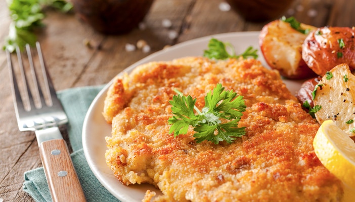 Wiener Schnitzel with roasted potatoes and lemon slice on a plate.