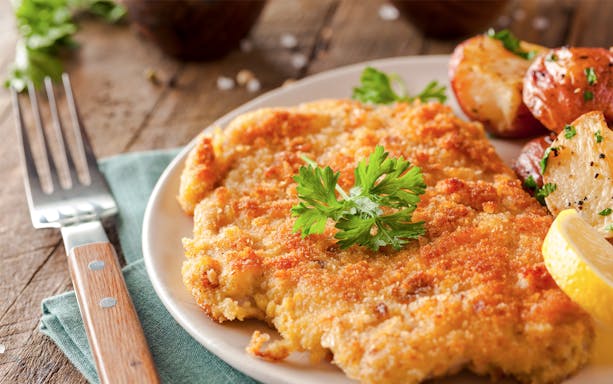Wiener Schnitzel with roasted potatoes and lemon slice on a plate.