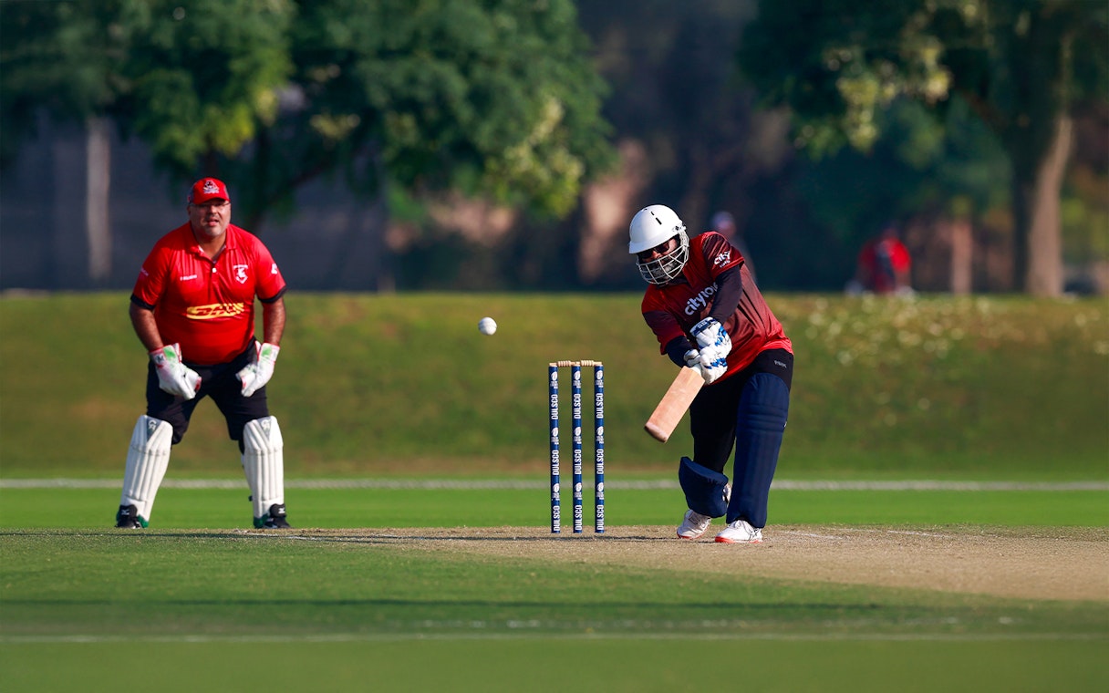 Cricket match at Emirates Dubai 7s with batsman hitting the ball and wicketkeeper ready.