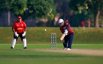Cricket match at Emirates Dubai 7s with batsman hitting the ball and wicketkeeper ready.
