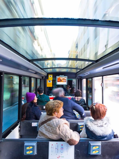 Tourists seated inside a glass-roofed bus in Granada, Spain.