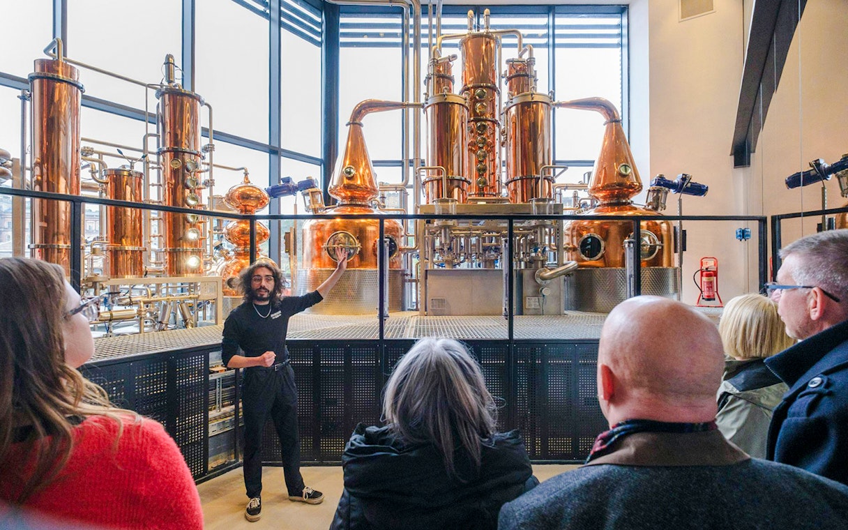 Tour guide explaining copper stills in the Still Room to visitors.
