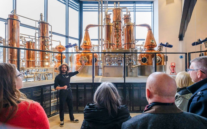 Tour guide explaining copper stills in the Still Room to visitors.