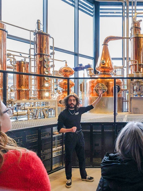 Tour guide explaining copper stills in the Still Room to visitors.