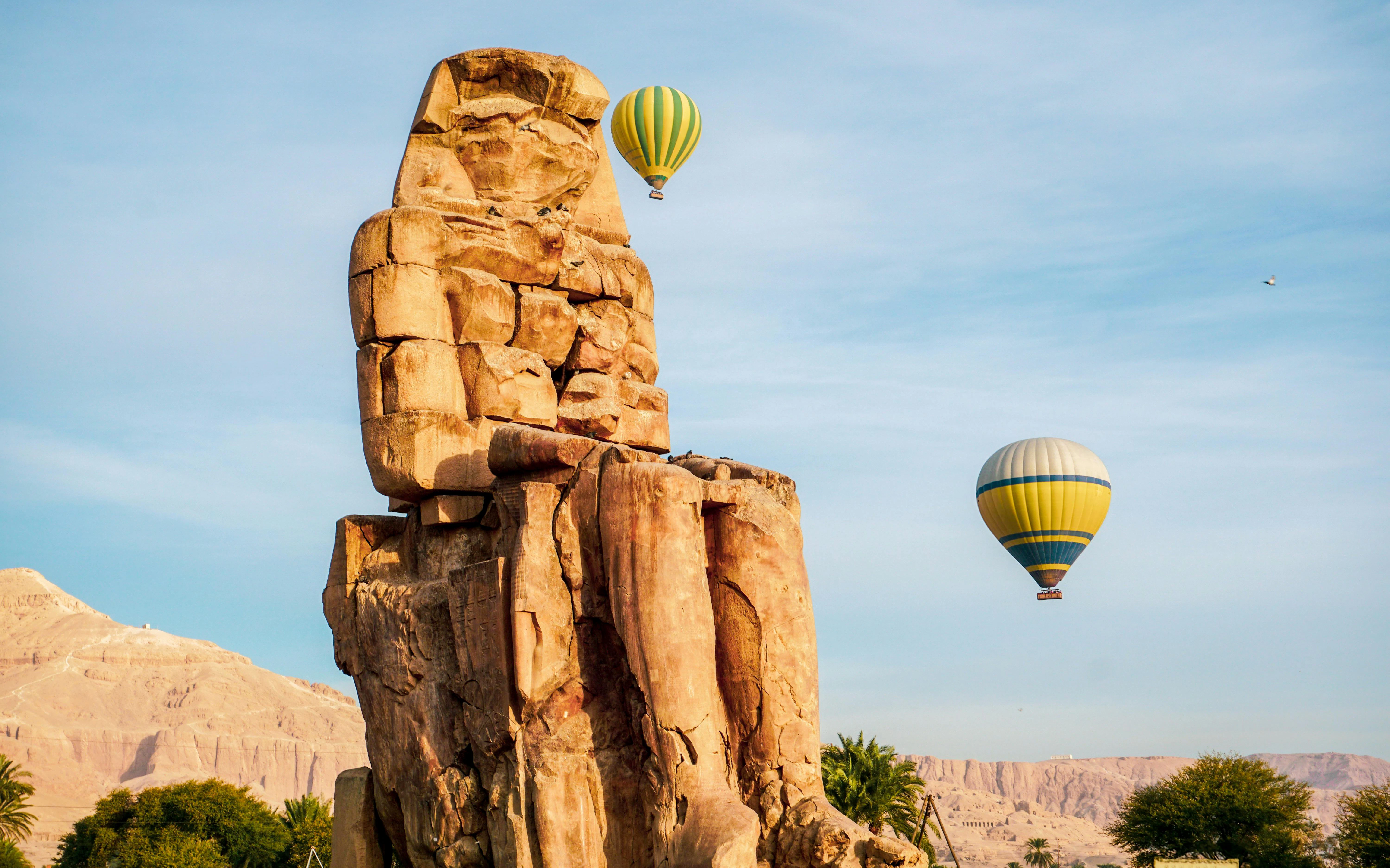 Colossi of Memnon with hot air balloons in Luxor, Egypt, against a blue sky.