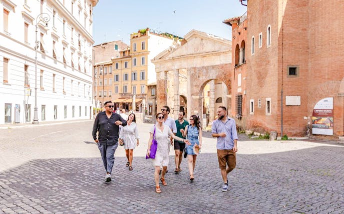 Tour group walking through the Jewish Ghetto neighborhood with ancient architecture in the background.