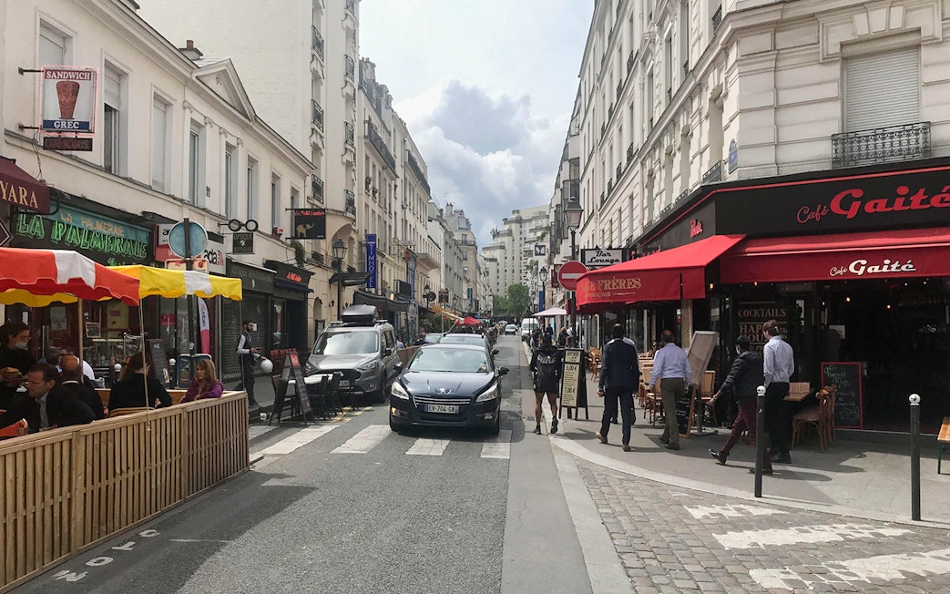 Pedestrians and cafes on a bustling street in Montparnasse, Paris during a walking tour.