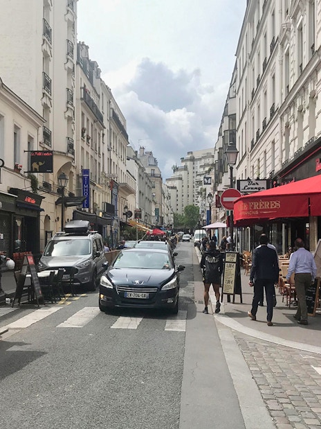 Pedestrians and cafes on a bustling street in Montparnasse, Paris during a walking tour.