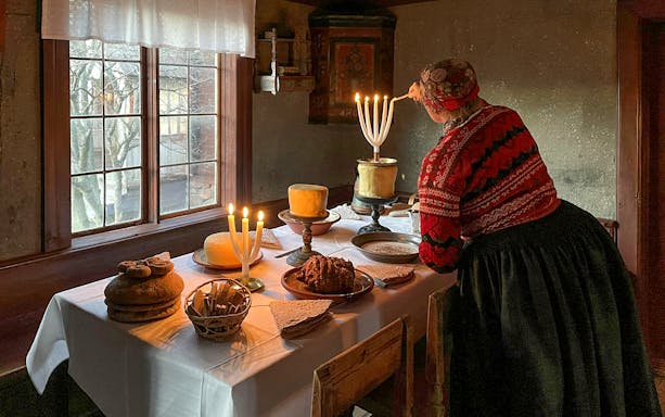 Person lighting candles on a table set with traditional Swedish food at Skansen Museum, Stockholm.