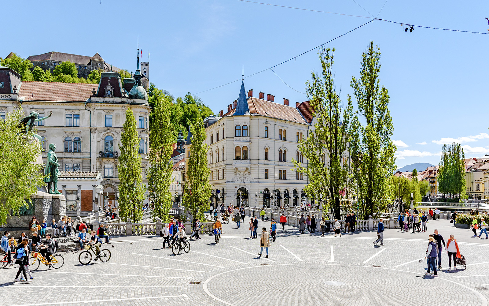 Prešeren Square in Ljubljana with people walking and cycling, featuring historic buildings and a statue.