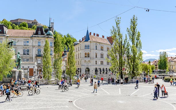 Prešeren Square in Ljubljana with people walking and cycling, featuring historic buildings and a statue.