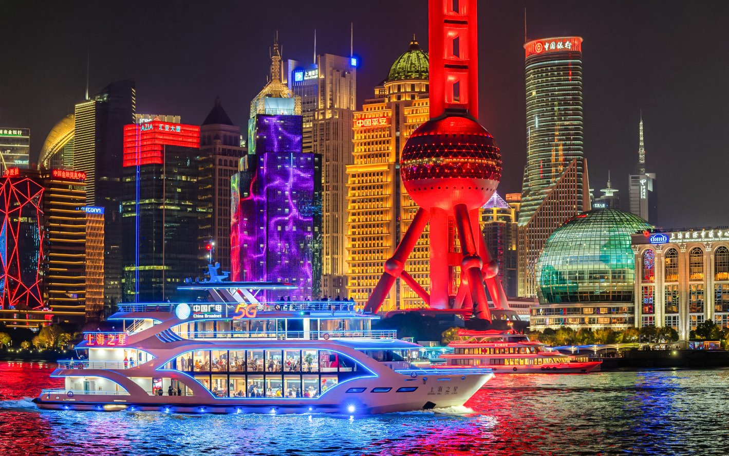 Cruise ship sailing past the illuminated Oriental Pearl Tower in Shanghai.