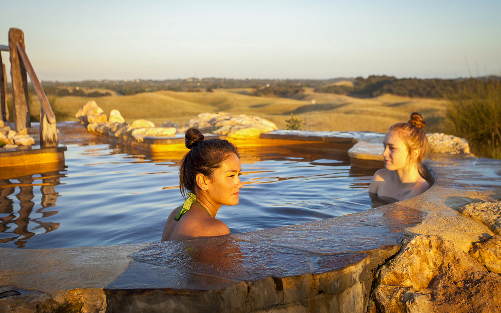 Visitors relaxing in a hot spring pool at Peninsula Hot Springs, surrounded by scenic landscape.