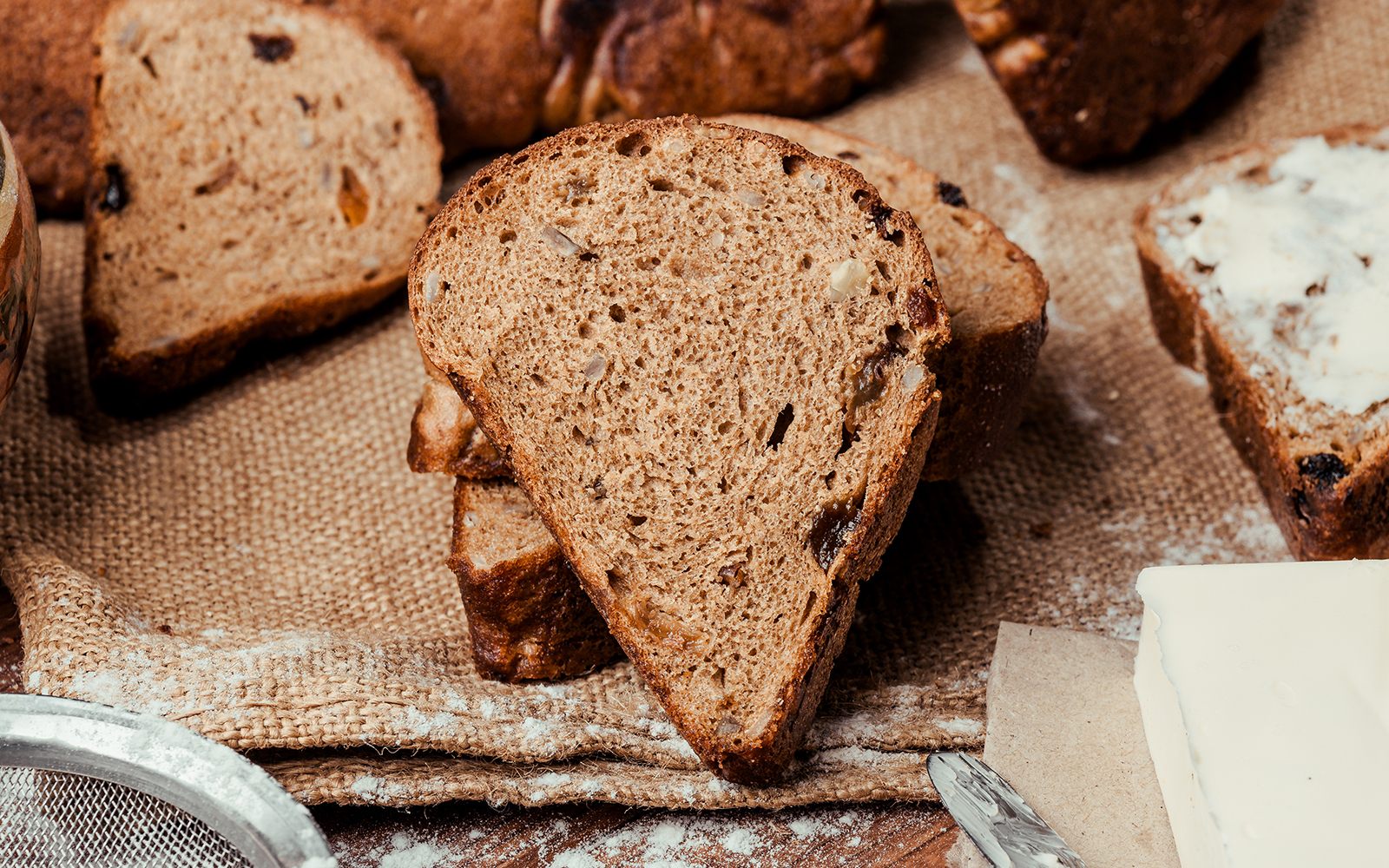 Two loaves of bread on a wooden background with raisins, dried apricots, sunflower seeds, caraway seeds.