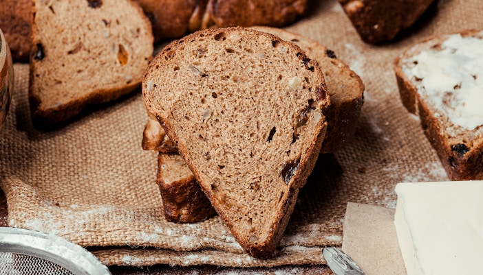 Two loaves of bread on a wooden background with raisins, dried apricots, sunflower seeds, caraway seeds.