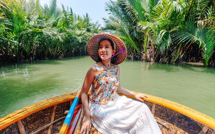 Woman enjoying basket boat tour on a lush green lagoon in Hoi An.