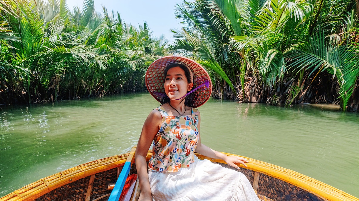 Woman enjoying basket boat tour on a lush green lagoon in Hoi An.