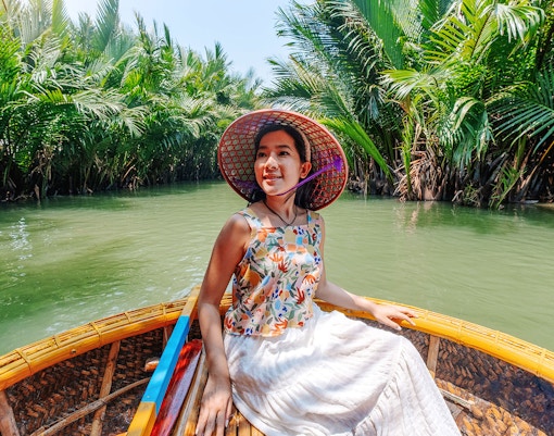 Woman enjoying basket boat tour on a lush green lagoon in Hoi An.