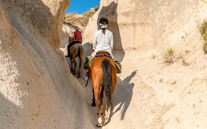 Horseback riders navigating narrow valley in Cappadocia, Turkey.