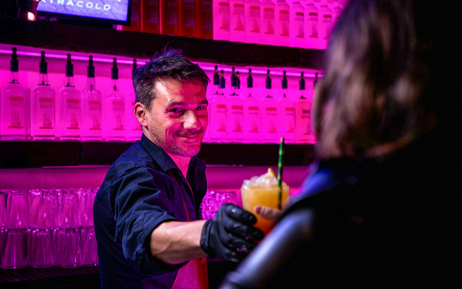 Bartender serving a cocktail at Icebar Amsterdam with vibrant lighting.