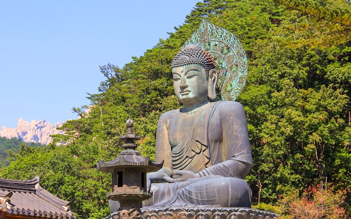 Buddha statue at Seoraksan Sinheungsa Temple surrounded by trees and mountains.