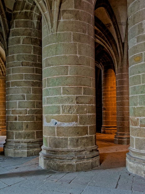 Great pillar hall in Mont Saint Michel with towering columns and arched ceilings.