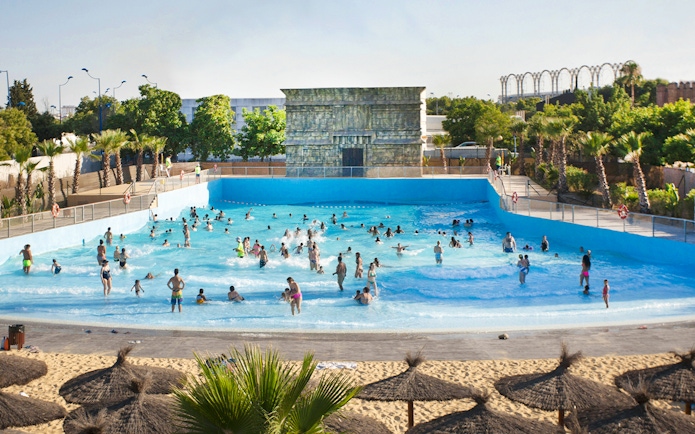 Visitors enjoying the wave pool at Isla Mágica, surrounded by palm trees and a sandy beach.