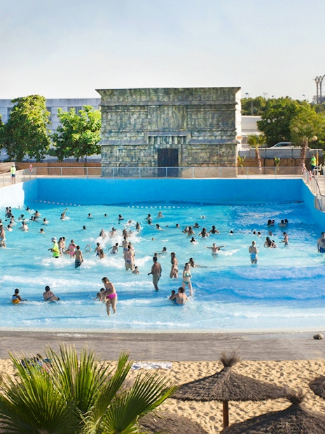 Visitors enjoying the wave pool at Isla Mágica, surrounded by palm trees and a sandy beach.