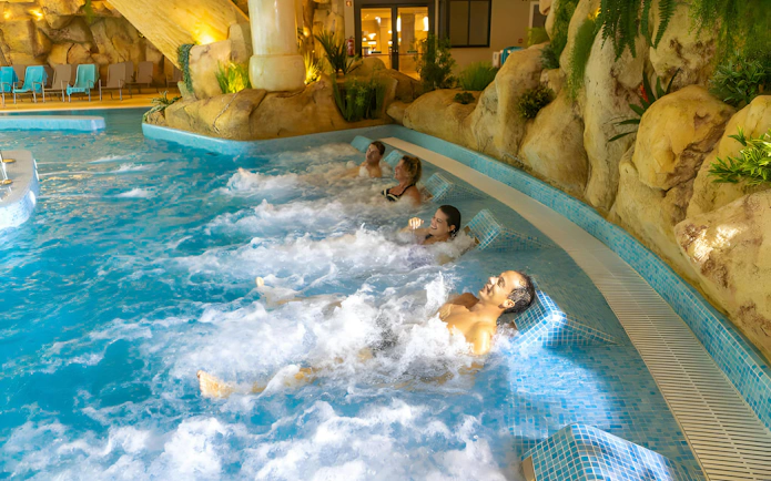 Visitors relaxing in a jacuzzi at Aquashow Indoor Park, surrounded by rock formations.