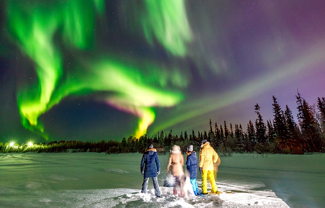 Group watching Northern Lights in snowy landscape near Reykjavik.