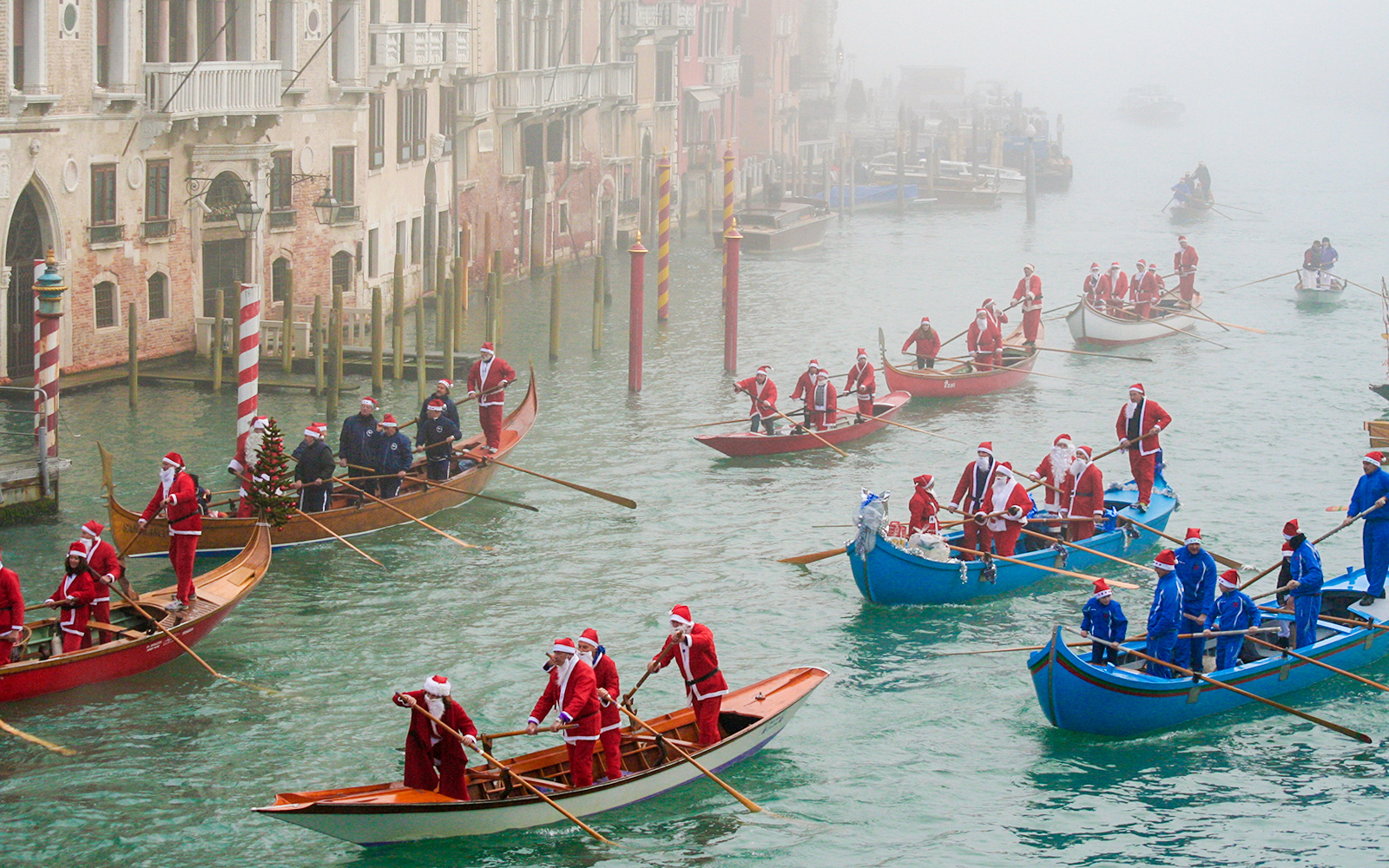 Santas rowing gondolas on a foggy canal in Venice during Christmas.