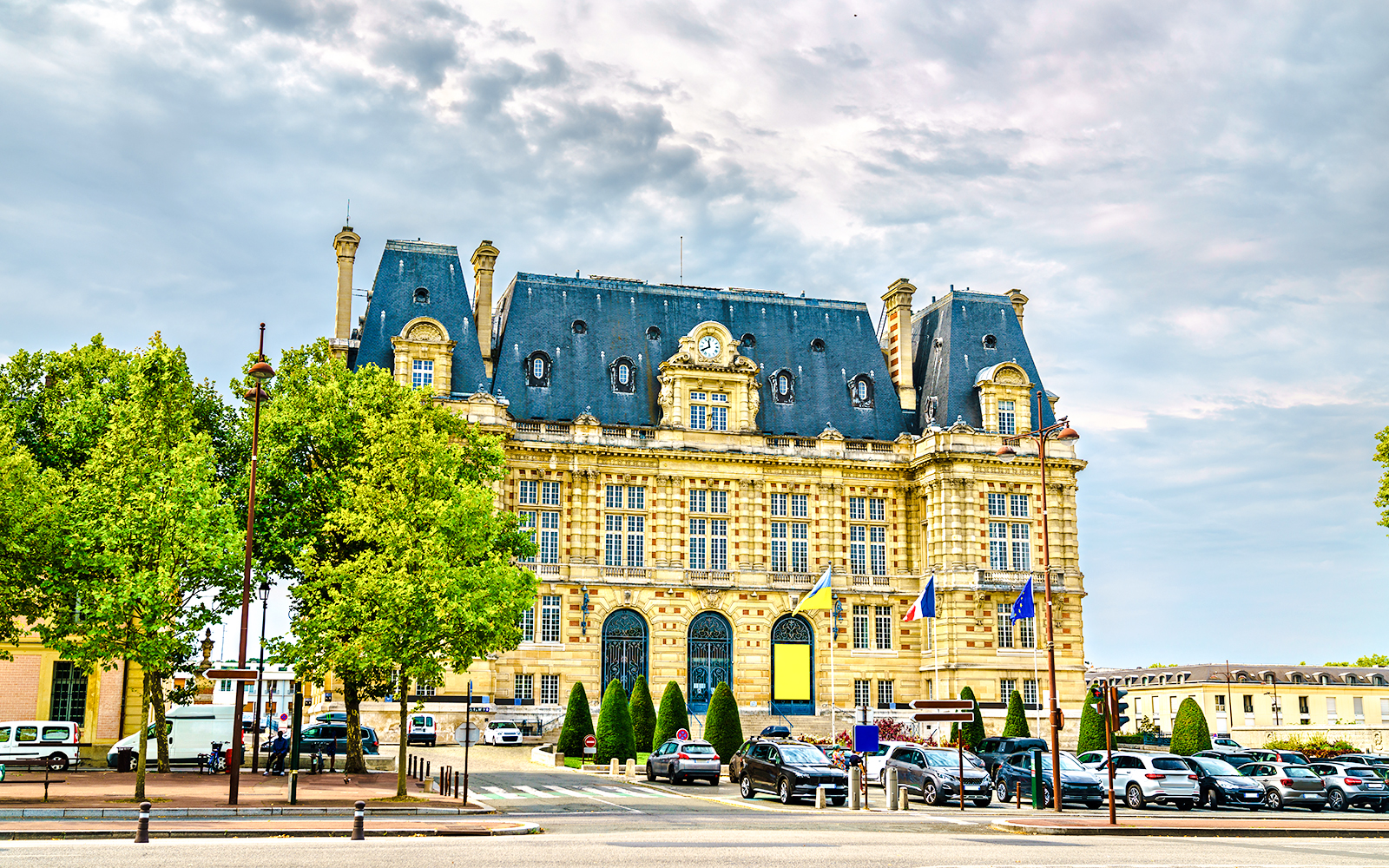 Versailles Town Hall with parked cars and surrounding trees.