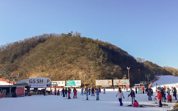 Skiers at Elysian Gangchon Ski Resort with snowy slopes and forested hills, near Seoul.