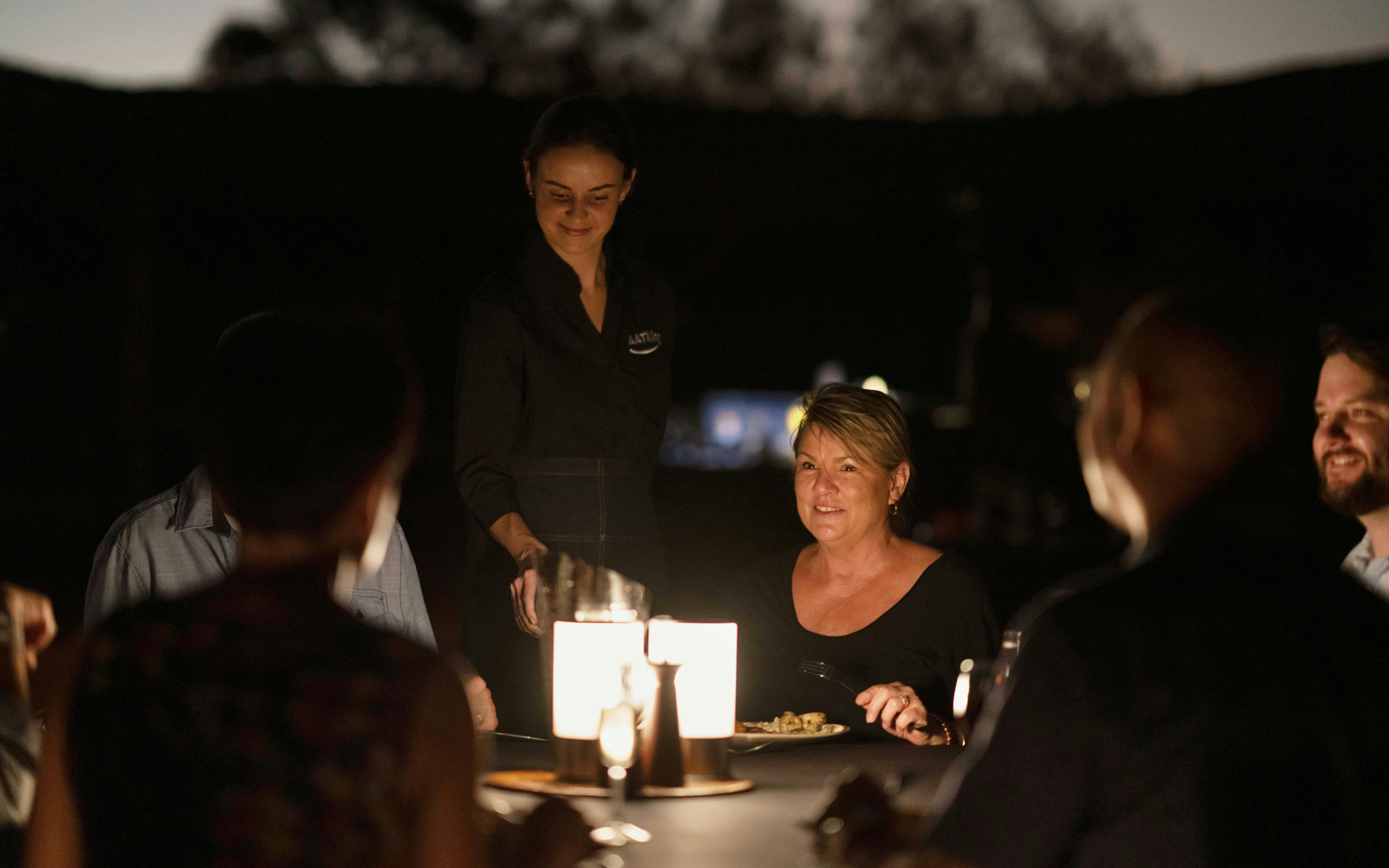 Guests dining outdoors during Uluru sunset tour with BBQ dinner.