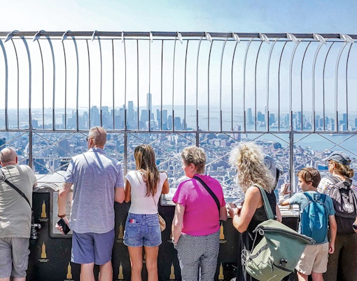 Visitors viewing New York City skyline from Empire State Building observatory.
