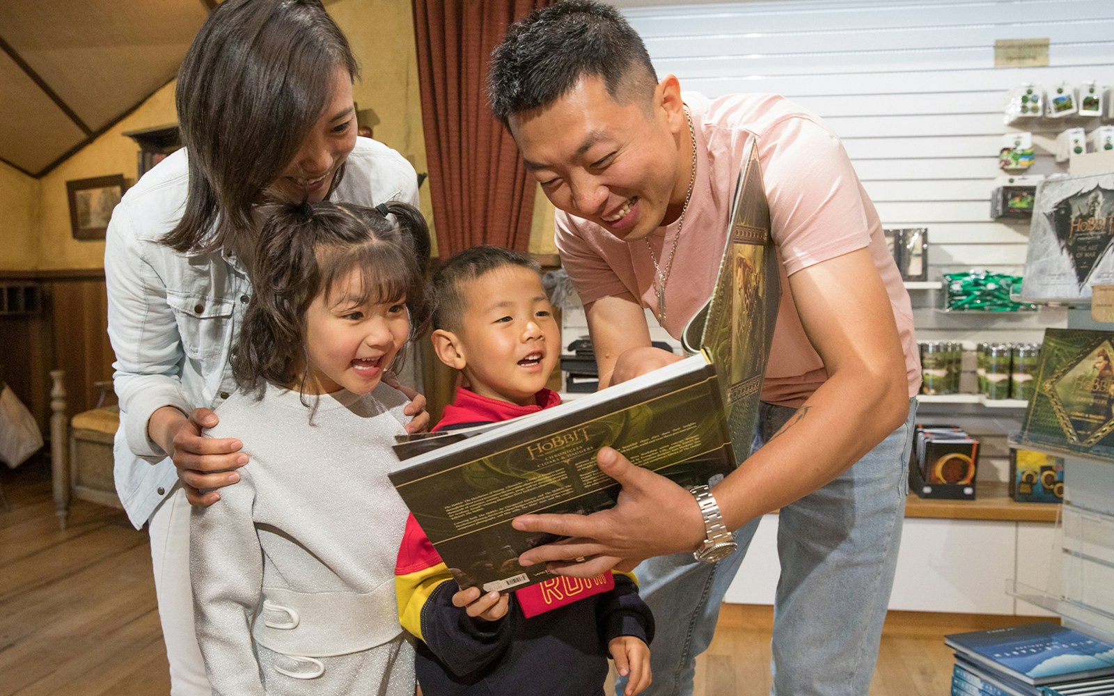 Family enjoying a book at Hobbiton Movie Set gift shop, New Zealand tour.