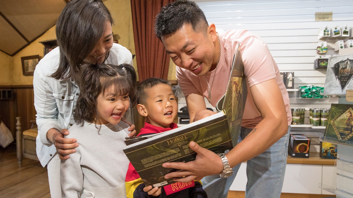 Family enjoying a book at Hobbiton Movie Set gift shop, New Zealand tour.