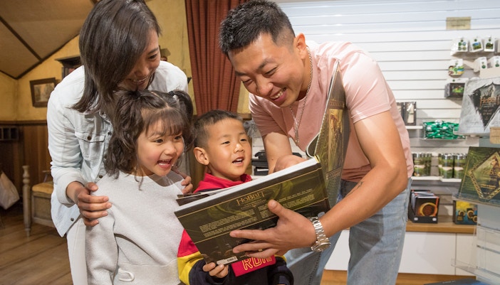 Family enjoying a book at Hobbiton Movie Set gift shop, New Zealand tour.