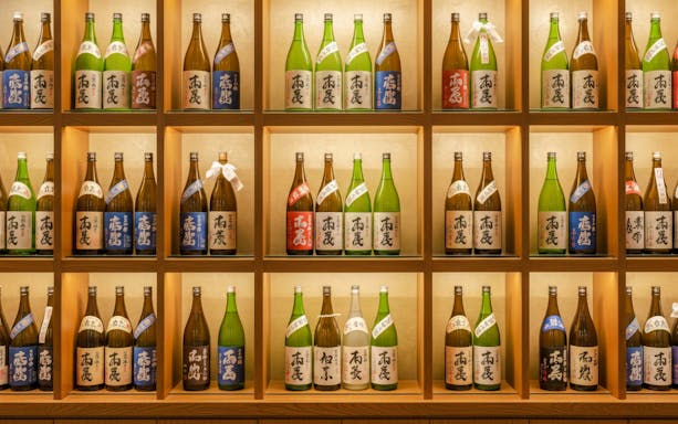 Sake bottles displayed on wooden shelves in a Japanese store.