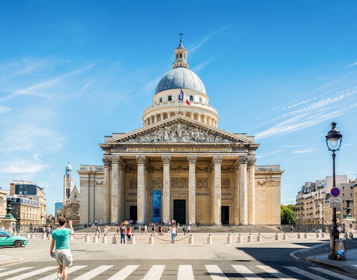 Pantheon in Paris with people walking in front, clear blue sky above.