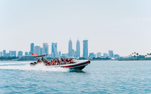 Speedboat with tourists in Dubai Marina, city skyline in background.