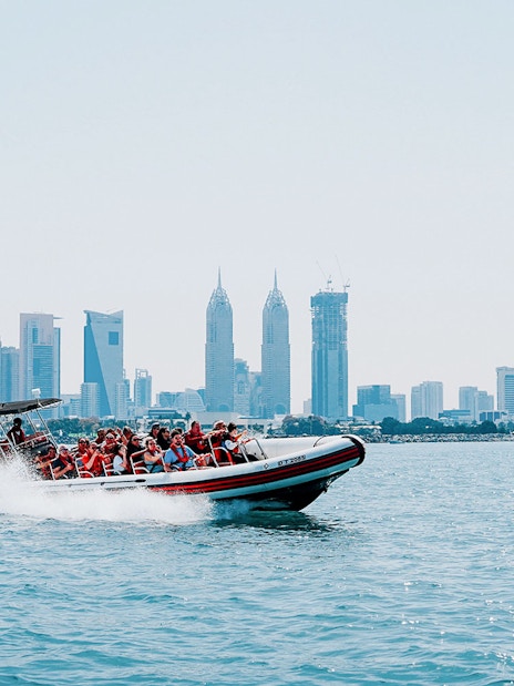 Speedboat with tourists in Dubai Marina, city skyline in background.