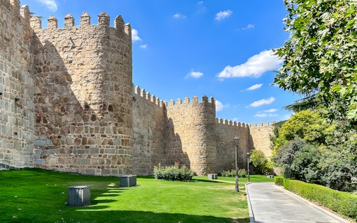 Medieval city walls of Ávila with stone towers and a grassy path.