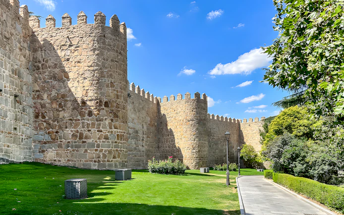 Medieval city walls of Ávila with stone towers and a grassy path.