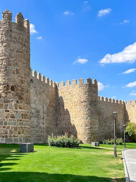 Medieval city walls of Ávila with stone towers and a grassy path.
