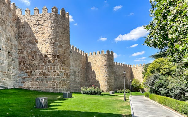 Medieval city walls of Ávila with stone towers and a grassy path.