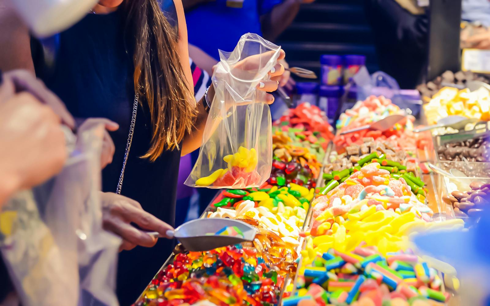 Customers selecting colorful jelly candies at a candy shop display.