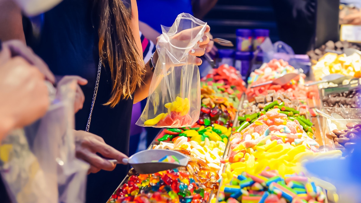Customers selecting colorful jelly candies at a candy shop display.