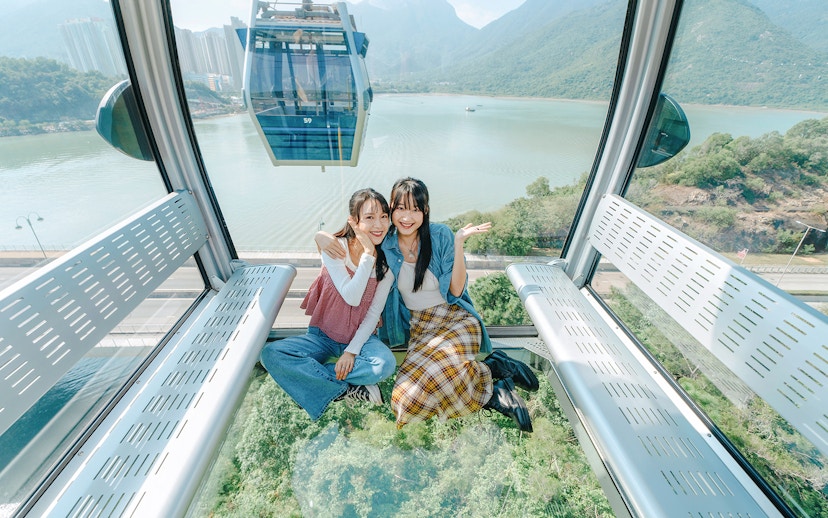 People enjoying a ride in a standard cable car at Ngong Ping, overlooking lush landscapes.